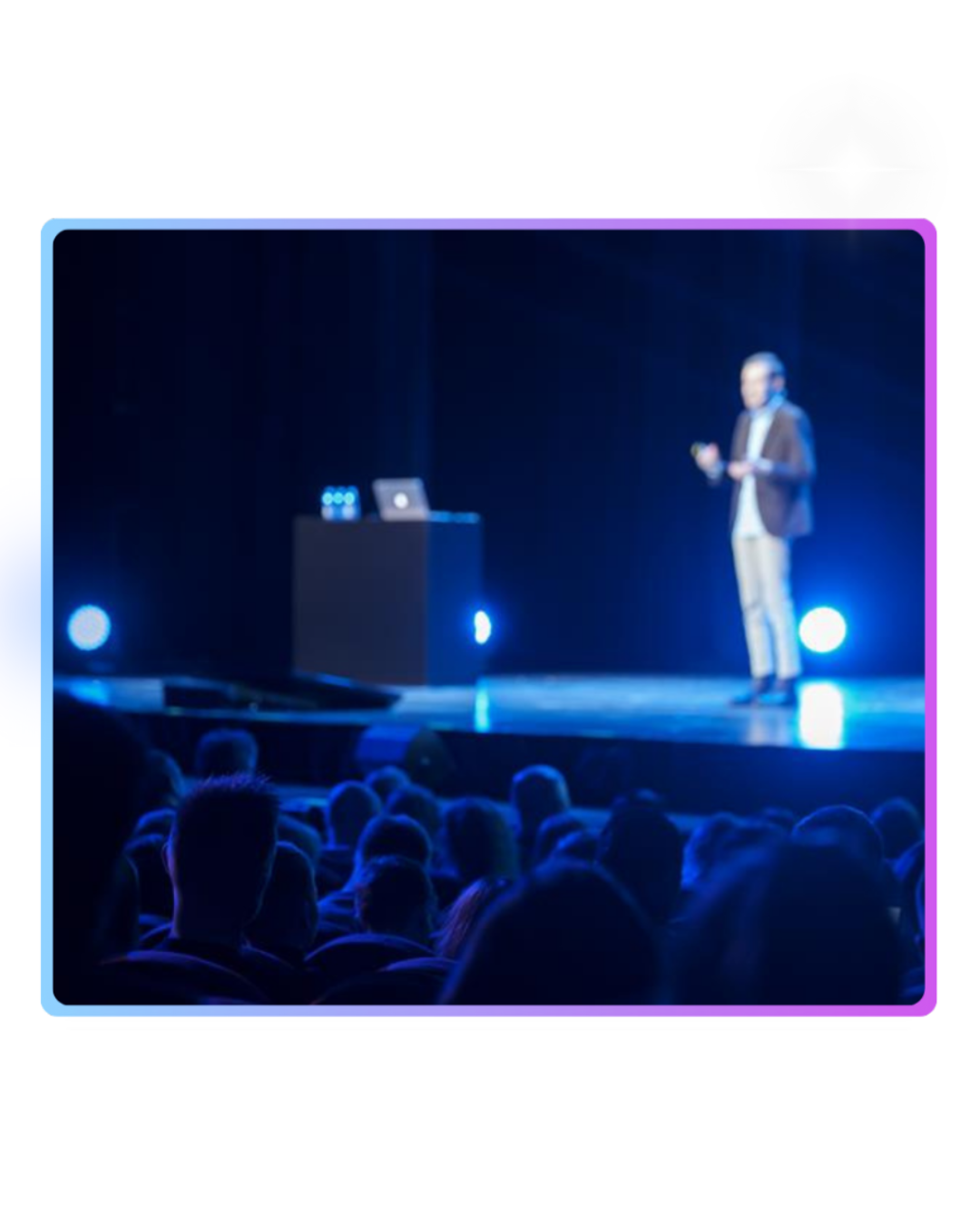 Speaker presenting on stage at a live event with an audience seated in front, under blue lighting.
